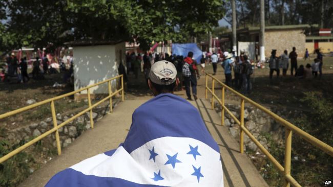 Un inmigrante con bandera hondureña cruza un puente en México.